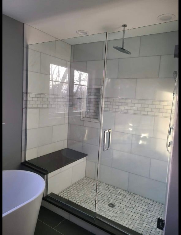 Modern glass shower with tiled walls and a built-in bench, next to a freestanding bathtub.