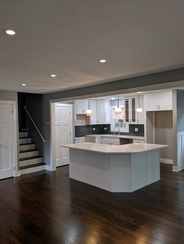 Modern kitchen with white cabinets, island, and dark hardwood floors, adjacent to a staircase.